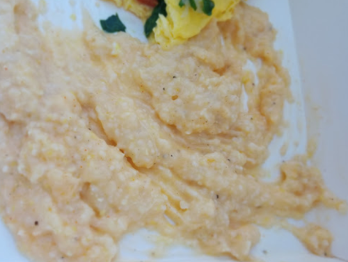 A close-up of creamy, yellow grits served with a side of scrambled eggs and garnished with herbs.