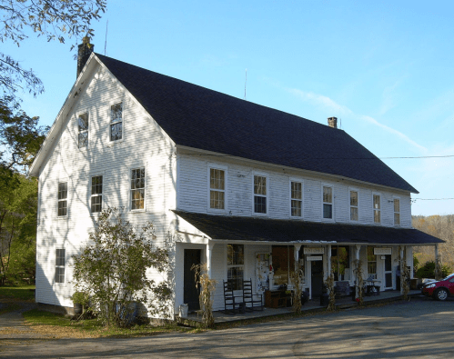 A white, two-story building with a sloped roof, featuring multiple windows and a porch, set against a clear blue sky.