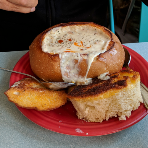 A bowl of creamy soup served in a bread bowl, accompanied by toasted bread slices on a red plate.