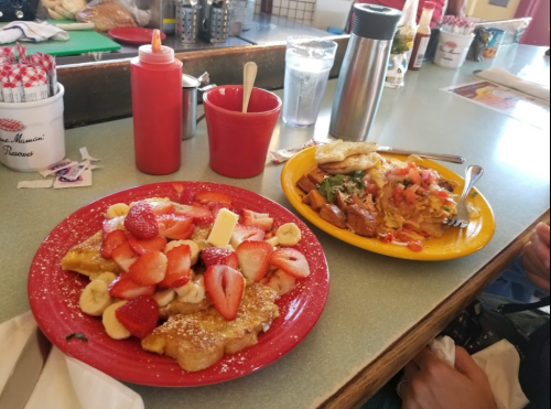 A colorful breakfast spread featuring French toast topped with strawberries and bananas, alongside a savory dish with eggs and potatoes.