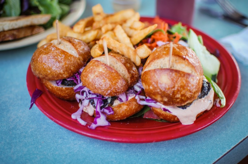 Three mini sandwiches with coleslaw on a red plate, accompanied by fries and a side salad.