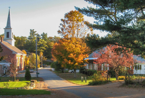 A quaint street scene with a church, colorful autumn trees, and charming houses under a clear sky.