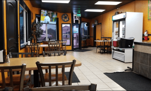 Interior of a casual dining restaurant with tables, a TV, a drink cooler, and an entrance visible.