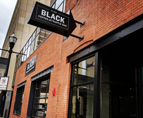 Exterior of a brick building featuring a sign for "BLACK Coffee and Waffle Bar" with a modern design.