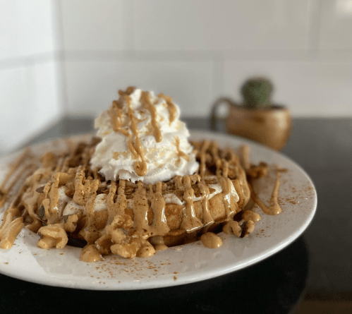 A delicious waffle topped with whipped cream, drizzled with caramel, and sprinkled with nuts on a white plate.