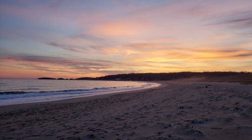 A serene beach at sunset, with gentle waves and colorful skies reflecting on the water.