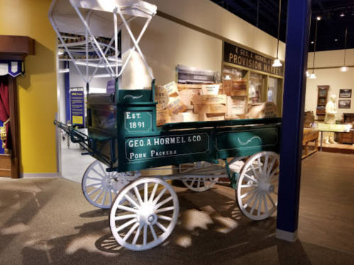 A vintage green delivery wagon with white wheels, marked "Geo. A. Hormel & Co. Pork Packers," displayed indoors.