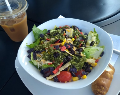 A colorful salad with lettuce, tomatoes, corn, black beans, and tortilla strips, alongside a drink and a pastry.