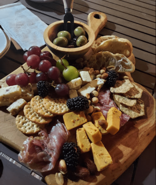A wooden platter filled with assorted cheeses, meats, crackers, grapes, olives, and nuts.
