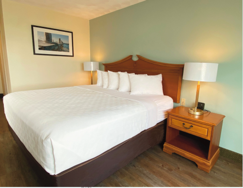 A cozy hotel room featuring a queen bed with white linens, a wooden headboard, and a bedside table with a lamp.