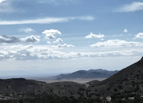 A scenic view of rolling hills and a vast landscape under a cloudy sky.