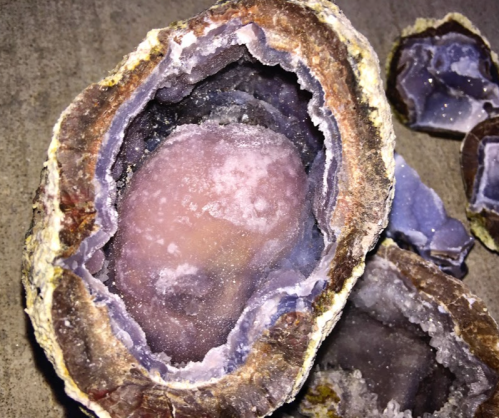 A geode with a purple and clear crystal interior, surrounded by rough, textured rock.
