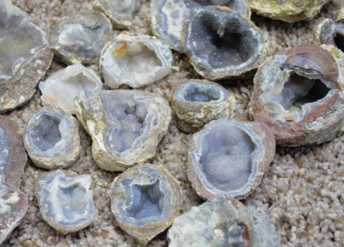 A collection of geodes with gray and white crystals, scattered on a textured surface.