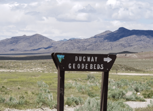 Signpost for Dugway Geode Beds with mountains and a cloudy sky in the background.