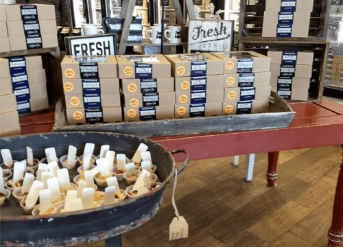 A display of baked goods in boxes and small cups, with a rustic table and signs reading "Fresh" and "Fresh Baked."