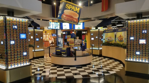 Interior of a SPAM-themed restaurant with checkered floors, colorful displays, and a large SPAM burger sign.