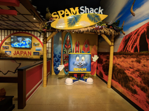 A colorful entrance to the SPAM Shack featuring a cartoonish SPAM character and surfboards in a vibrant setting.