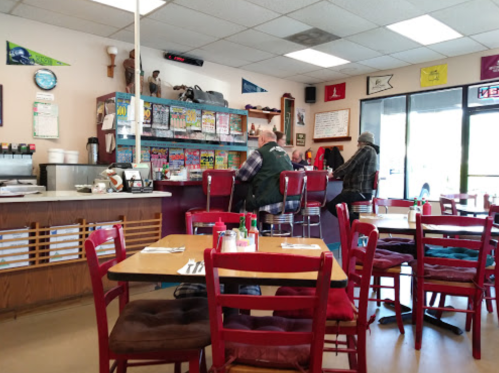 A cozy diner interior with red chairs, a counter, and patrons enjoying their meals. Colorful decor on the walls.