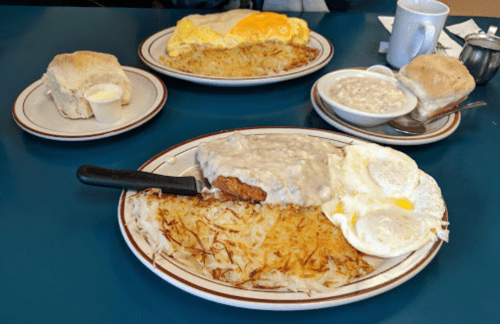 A plate with chicken fried steak, gravy, eggs, and hash browns, with biscuits and gravy on the side.