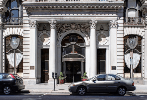 Elegant building entrance with tall columns, decorative details, and parked cars on the street.
