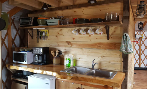 Cozy wooden kitchen with shelves of dishes, utensils, a coffee maker, and a double sink. Warm, rustic decor.