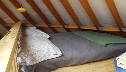 Cozy attic bedroom with a wooden frame, featuring a bed covered in gray and green blankets under sloped ceilings.