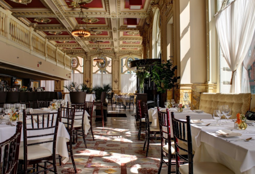 Elegant restaurant interior with ornate decor, large windows, and tables set for dining. Bright and inviting atmosphere.