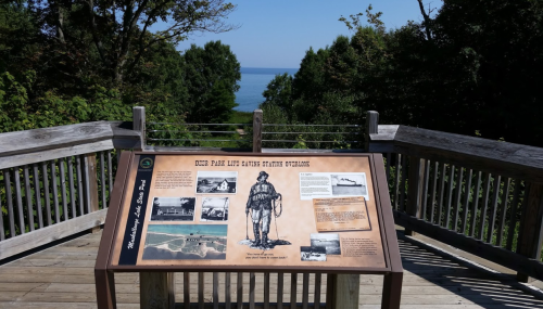 A wooden viewing platform with an informational sign overlooking a lake and surrounded by trees.