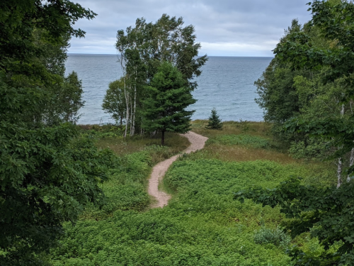 A winding path through lush greenery leads to a serene lake under a cloudy sky.