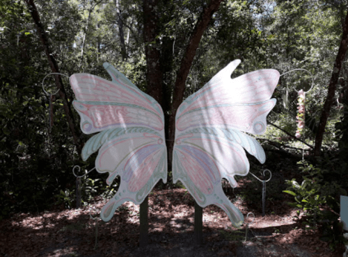 A large, colorful butterfly sculpture with open wings, set in a lush, green forest environment.