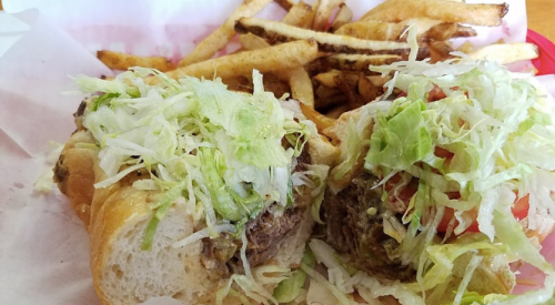 A close-up of a sandwich filled with lettuce and tomato, served with a side of golden French fries.