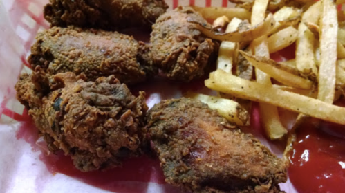 A basket of crispy fried chicken wings with a side of golden French fries and ketchup.