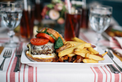 A plate with a cheeseburger topped with tomato and lettuce, served with crispy fries, on a striped tablecloth.
