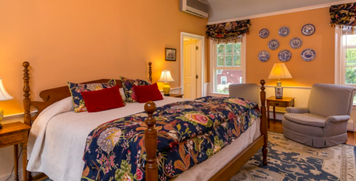 Cozy bedroom with orange walls, a large bed with decorative pillows, and a comfortable armchair by the window.