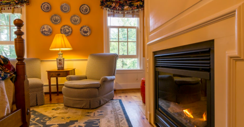Cozy room with orange walls, two armchairs, a lamp, decorative plates, and a fireplace. Warm and inviting atmosphere.