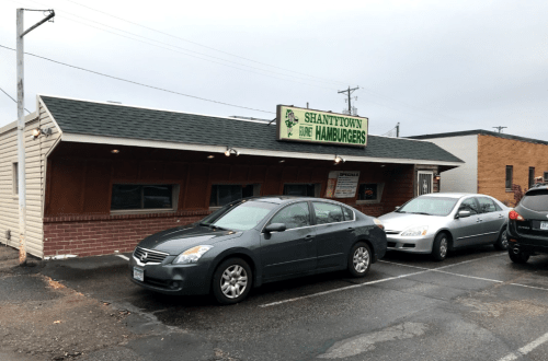 Exterior of Shantytown Hamburgers restaurant with parked cars in front on a cloudy day.