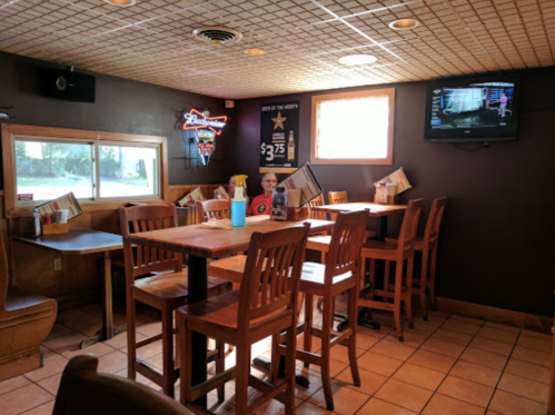 A cozy restaurant interior with wooden tables and chairs, a TV on the wall, and a window letting in natural light.