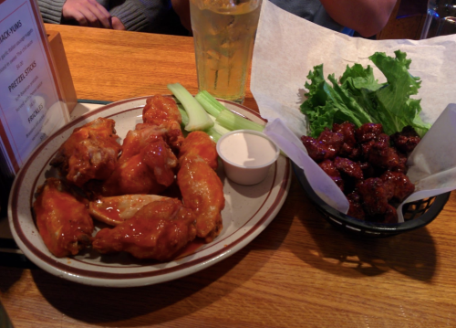 A plate of chicken wings with celery and dipping sauce, alongside a basket of crispy wings on lettuce.