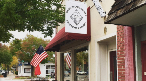 A cozy café with a sign for Windsor Lake Coffee, Ice Cream & Bakery, featuring an American flag and autumn foliage.