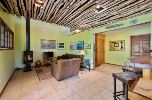 Cozy living room with a rustic ceiling, wood stove, and comfortable seating, featuring green walls and artwork.