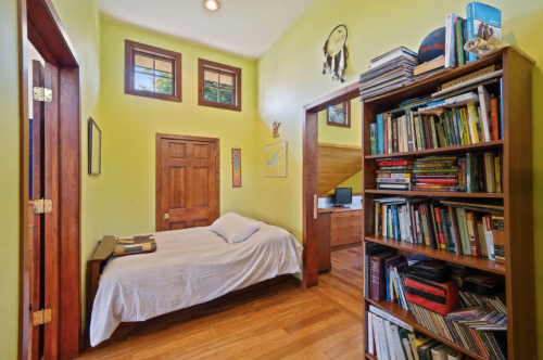 Cozy bedroom with green walls, a bed, wooden bookshelf filled with books, and a small desk in the background.