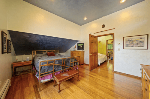 Cozy bedroom with a sloped ceiling, wooden furniture, and a doorway leading to another room. Warm lighting enhances the space.