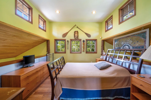 Cozy bedroom with green walls, wooden accents, a bed, and decorative items, featuring large windows for natural light.