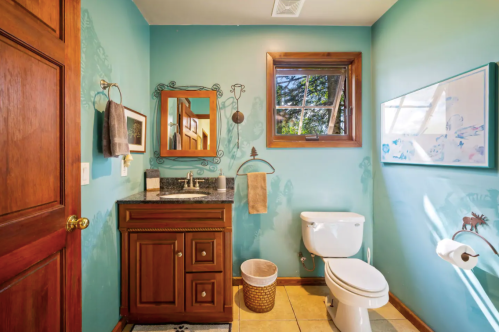 Bright bathroom with teal walls, wooden accents, a mirror, sink, and a window letting in natural light.