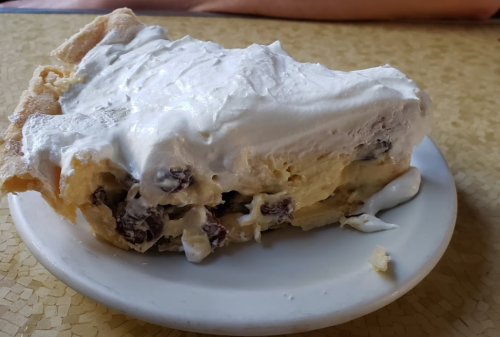 A slice of cream pie topped with whipped cream, sitting on a small white plate.