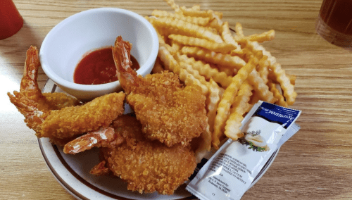 A plate of crispy fried shrimp with a side of crinkle-cut fries and a small bowl of dipping sauce.