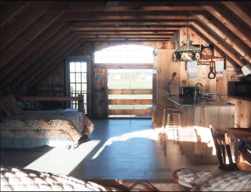 Cozy wooden attic space with two beds, a kitchenette, and large windows letting in natural light.