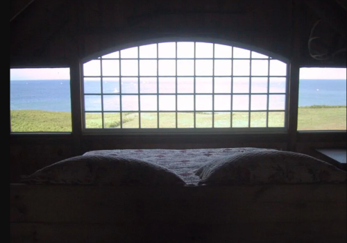 A cozy bed with a view of a serene landscape and ocean through a large window.