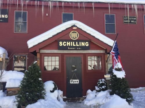 A red building with a sign reading "Schilling Beer Co." and an American flag, surrounded by snow and icicles.