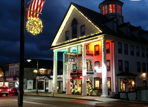 Historic building decorated with colorful lights, featuring a large porch and festive holiday decorations at dusk.